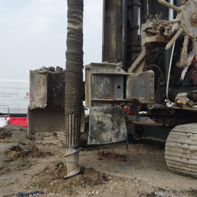 Rigid Inclusions Being Installed By A Large Drilling Rig For At St Modwen Park, Burton. A Worker In PPE Stands Beside The Rig And Examines Paperwork.