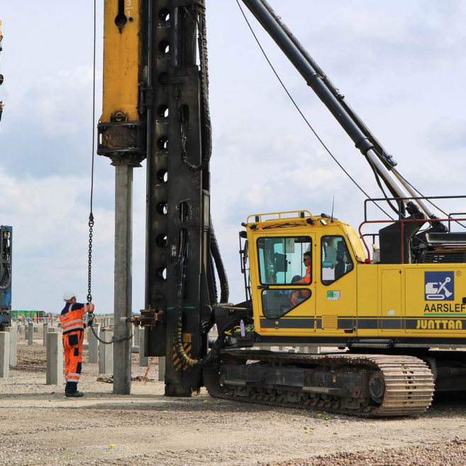 Aarsleff's Junttan PM 20HLC piling rig in operation with two workers present. Another piling rig can be seen in the background.