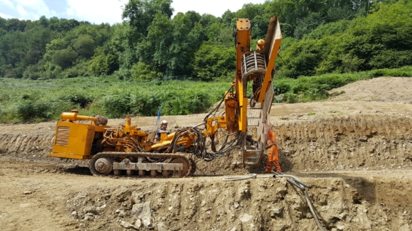 Aarsleff's rig be used to install soil nails for Elan Valley Aqueduct Rehabilitation project. Two workers are visible, one operating the machine, the other assisting on the ground.