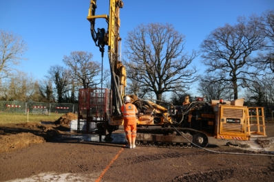 Aarsleff worker in safety gear near a yellow drilling rig on a construction site under a clear blue sky.