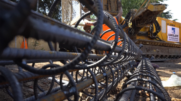 Close-up view of steel reinforcement cages at a construction site. A yellow KLEMM drilling rig is in the background.