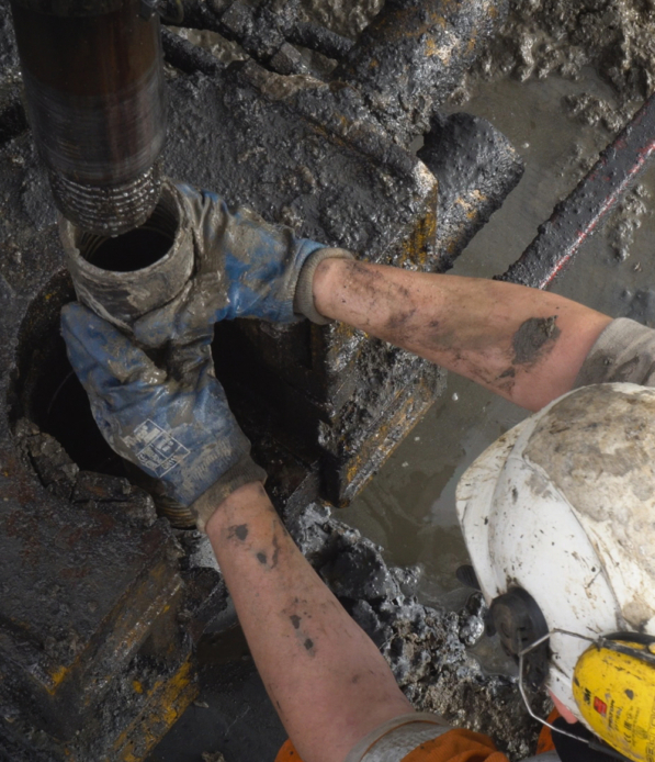 A worker wearing PPE handles a pipe on muddy site.
