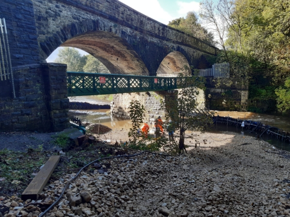 Workers in orange hi-vi clothing stand under a bridge and examine the riverbed area.