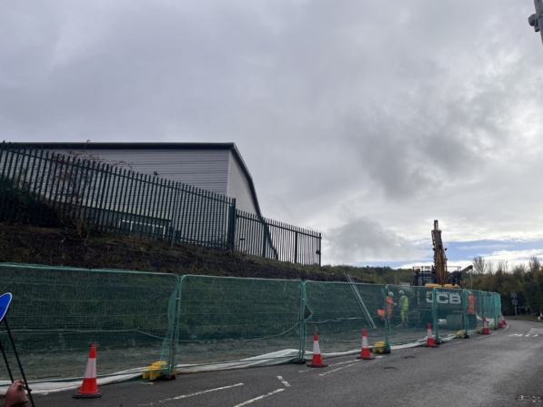 A soil nailed solution being constructed by Aarsleff in Northampton. A JCD machine, workers, a temporary fence and traffic cones are visible.