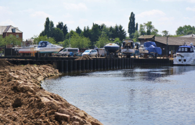 Boats on land and in water at Newark Marine on a sunny day. A rocky shoreline is shown in the foreground.