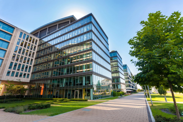 Modern, multi-story commercial buildings under a blue sky. The structures feature glass exteriors and well-maintained landscaping.
