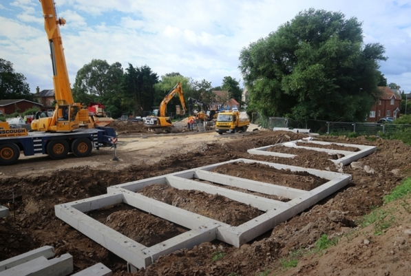 Square concrete foundations on a residential construction site. Yellow heavy machinery can be seen in the background.