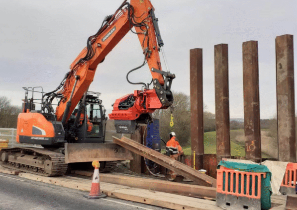 An excavator is shown driving sheet piles into the ground during the River Doe Lea project.