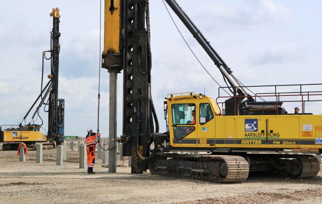 Aarsleff's Junttan PM 20HLC piling rig in operation with two workers present. Another piling rig can be seen in the background.