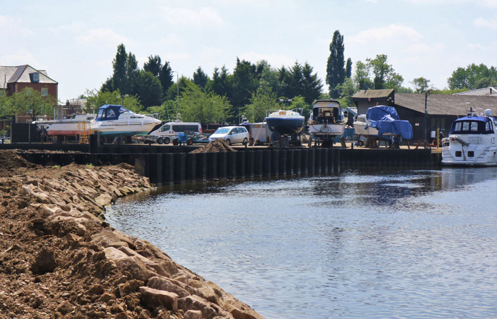 Boats on land and in water at Newark Marine on a sunny day. A rocky shoreline is shown in the foreground.