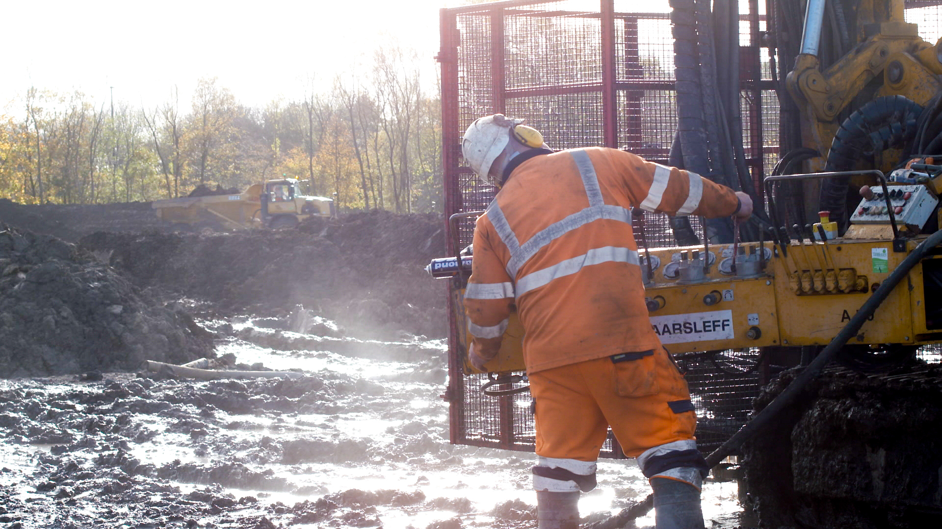 A skilled drilling and grouting contractor in an orange safety suit operating a drilling machine for soil engineering and soil stabilization in civil engineering projects.